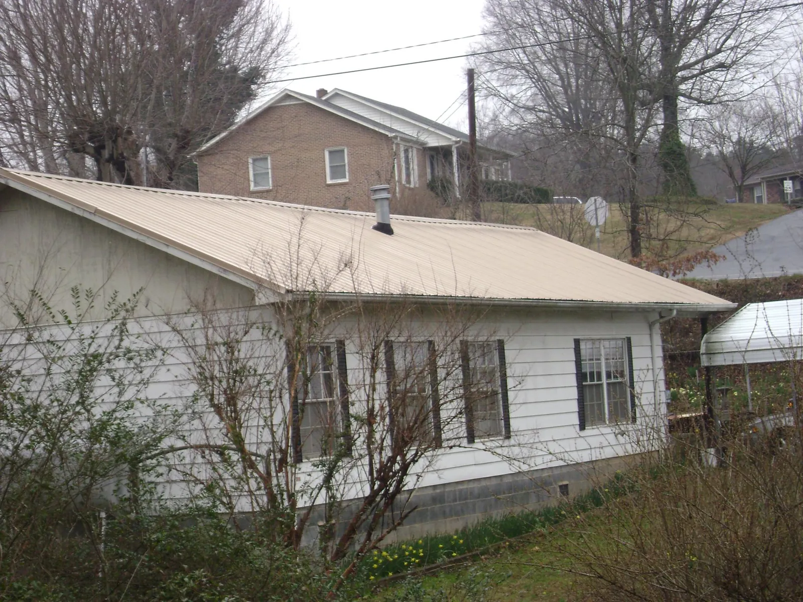 Tan metal roof on a white sided house set into a hillside — Commercial Roofing by Roofing Brothers in Eastport